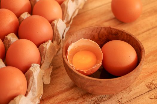 Cracked egg in bowl and egg shells on wooden table.