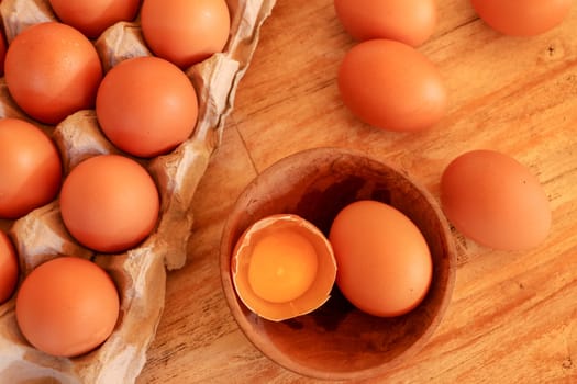 Cracked egg in bowl and egg shells on wooden table.