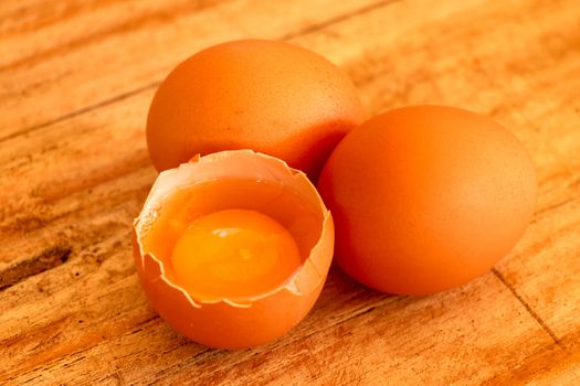 whole and broken brown eggs closeup on wooden background.