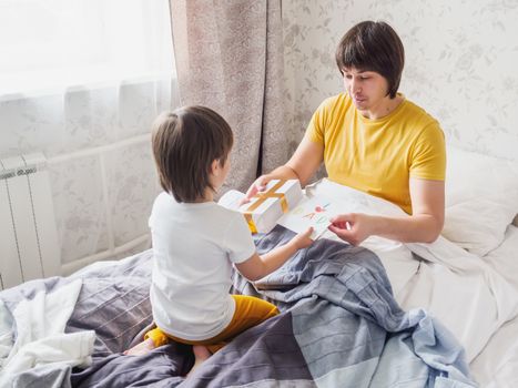 Happy Father's Day. Toddler gives present and handmade greeting card to his dad. Joyful festive morning in cozy home.