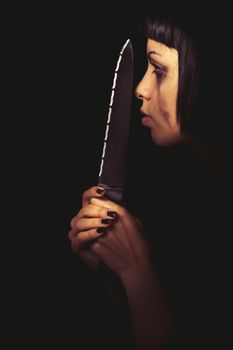 Killer profile. Murderous woman. Domestic crime. The profile of a young woman with a knife in her hand. In the darkness her face is illuminated. Crying. Home violence.