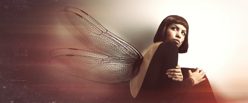 Delicate, feminine fragility. Young woman with wings. Conceptual and artistic image of a young girl with insect wings. Magical atmosphere like in a dream. The young woman is curled up.