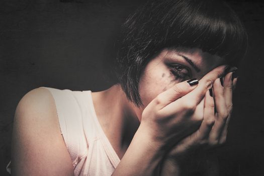 Young woman crying with her hands in her face. Domestic violence. Drained makeup.