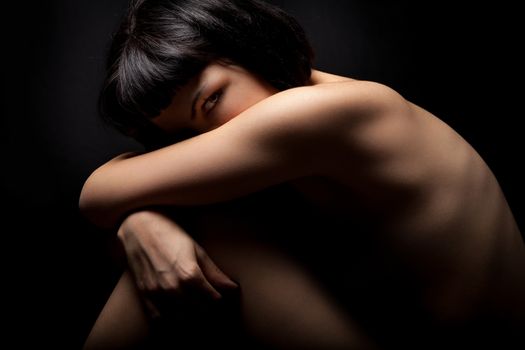 Naked girl, woman curled up in protection on black. Female health. Young woman curled up in protection on black. Black background.