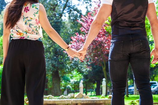 Loving engaged couple walking hand in hand, seen from the back with narrow shot. Two people, man and woman, hold hands outdoors.