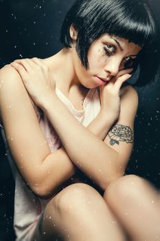 A young woman is crying. Makeup running. Tears, sadness and sweetness. Stardust. Blacks hair with bangs. Black background.