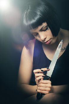 Murderous suicide girl with knife. Crime concept. A beautiful girl with a knife in hand has just committed a crime. Touching the blade watching the knife. On knife reflected her look with open eyes.