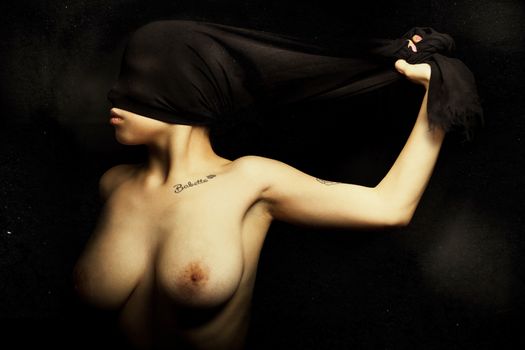 A young woman is blinded by a cloth pulled from hand. Artistic portrait with grunge background. Breasts exposed. Rebellion, silent, femininity, darkening, shame and women's empowerment concept.