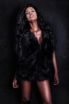 Beautiful young African American seductive black model woman on dark background. An attractive young woman wearing a furry black vest. Sensual look and perfect physique.