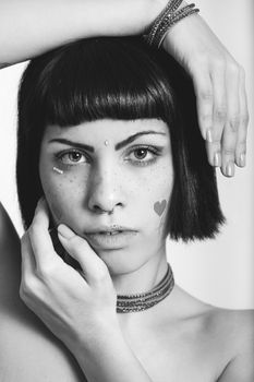 Portrait of young woman with freckles and heart-shaped stickers. Hands geometric position. Black and white