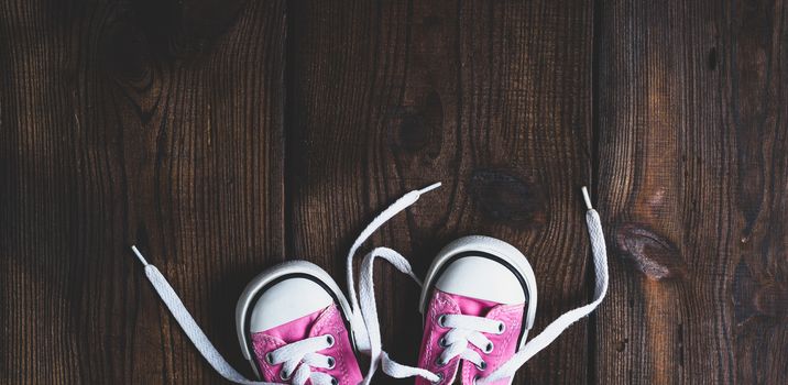 small pink textile sneakers on a brown wooden background, vintage toning, empty space