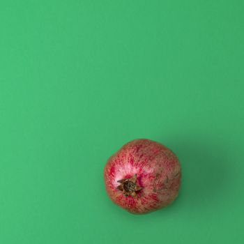 red pomegranate in the peel on a green background, copy space