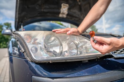 The man changes the bulb in the headlight of a car.