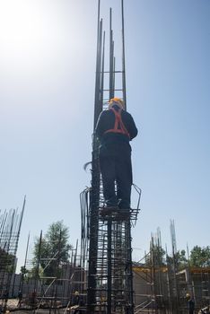 worker at altitude strengthens the pillars from rebar, on the blue sky background. candid, real people