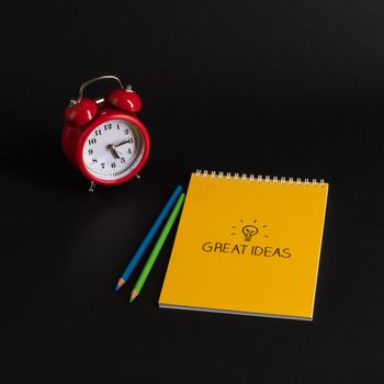 alarm clock with notepad and colored pencils on black background, isolated. back to school. great ideas