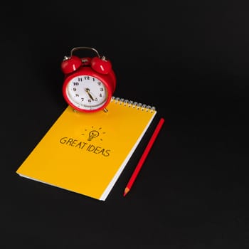 alarm clock with notepad and colored pencils on black background, isolated. back to school. great ideas