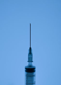 one medical syringe in an upright position on a light blue background