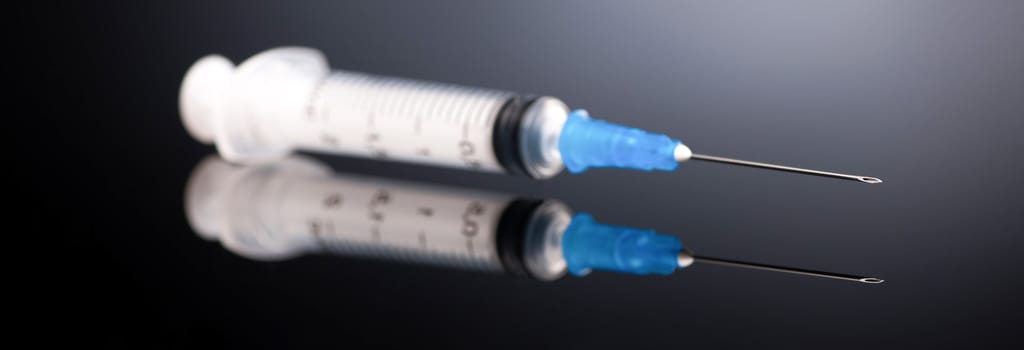 one medical syringe on a dark gray background with reflection