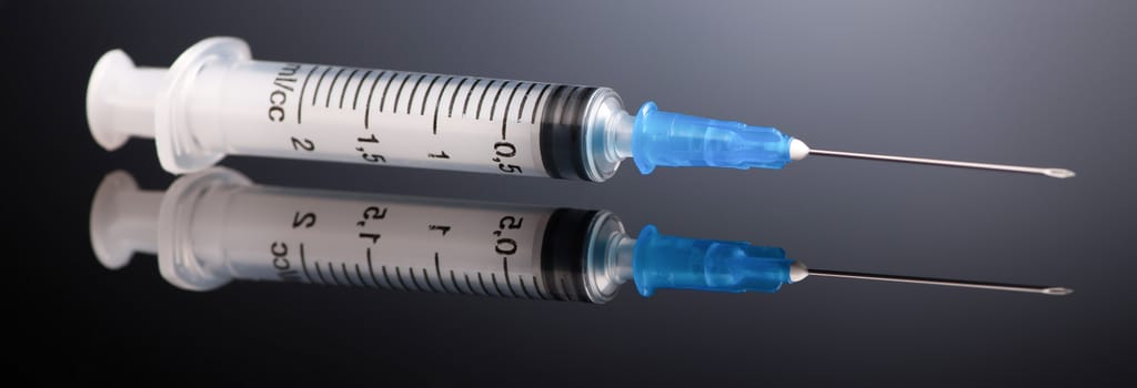 one medical syringe on a dark gray background with reflection