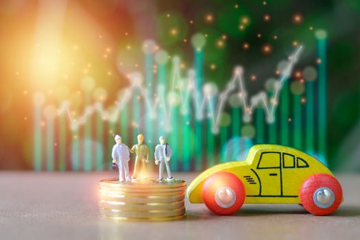 Group of engineer Miniature people, small model human figure standing on stack of golden coins and wooden yellow car  with green bokeh background. Copy space for your text. Business and financial concept.