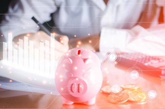 Business and analysis concept. Pink piggy bank on wooden table with white graph and chart icon analysis financial on virtual screen, positive growth of money and stock.