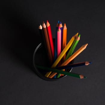 set of colored pencils in a basket on a black background, isolated. back to school
