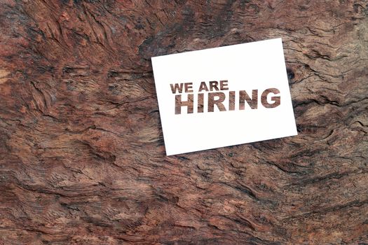 Cut the paper into text "WE ARE HIRING" on wooden background.