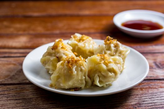 Chinese Steamed Dumpling, Shumai on white dish served with soy sauce on wooden table. Delicious Dimsum pork.