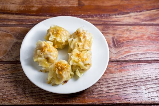 Chinese Steamed Dumpling, Shumai on white dish served with soy sauce on wooden table. Delicious Dimsum pork.