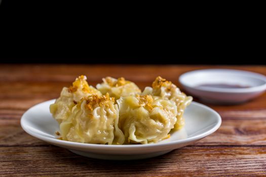 Chinese Steamed Dumpling, Shumai on white dish served with soy sauce on wooden table. Delicious Dimsum pork.