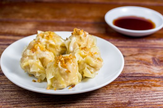 Chinese Steamed Dumpling, Shumai on white dish served with soy sauce on wooden table. Delicious Dimsum pork.