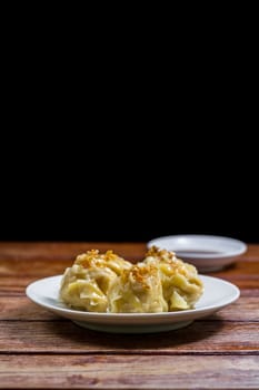 Chinese Steamed Dumpling, Shumai on white dish served with soy sauce on wooden table on black background. Delicious Dimsum pork.