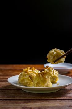 Chinese Steamed Dumpling, Shumai on white dish served with soy sauce on wooden table on black background. Delicious Dimsum pork.