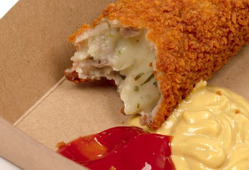 Partly eaten brown crusty dutch kroket with mustard and ketchup isolated on a white background