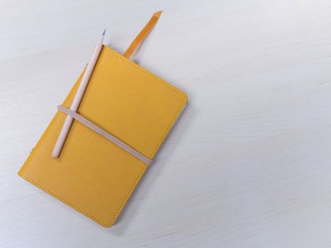 Top view of closed blank craft paper cover notebook with pencil on on wood table background