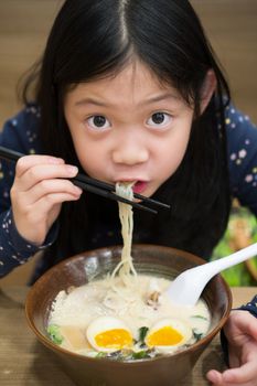 Little Asian girl eating a bowl of ramen.