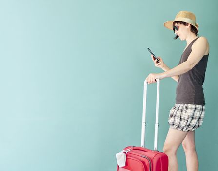 Woman in skirt, with straw hat and striped shirt prepared with a red suitcase and her face mask for her vacation in Covid's time