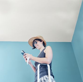 Woman in skirt, with straw hat and striped shirt prepared with a red suitcase and her face mask for her vacation in Covid's time