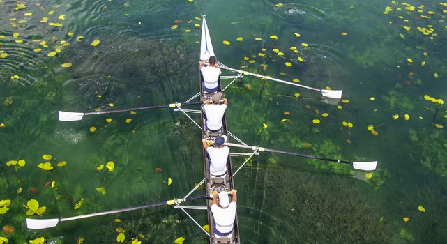 Men's quadruple rowing team on turquoise green lake
