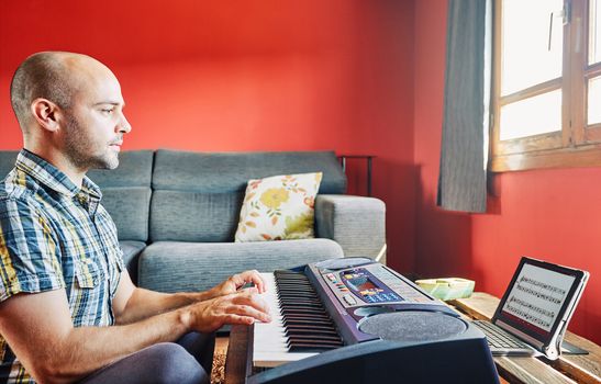 Man playing piano while taking online lessons at home.