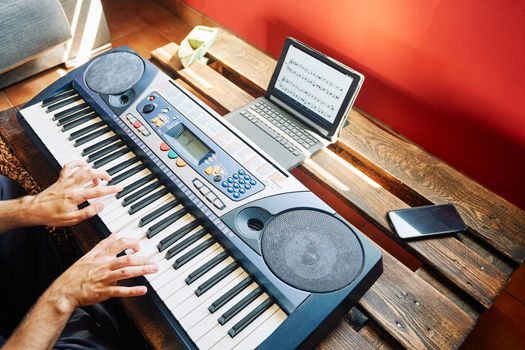 A man playing the piano at home while using a tablet to read the scores