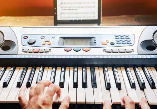 Man playing piano at home while using a tablet to read the scores