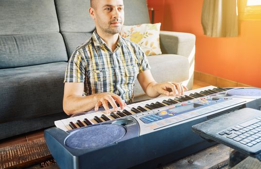 A man learning to play the piano while watching an online course at home