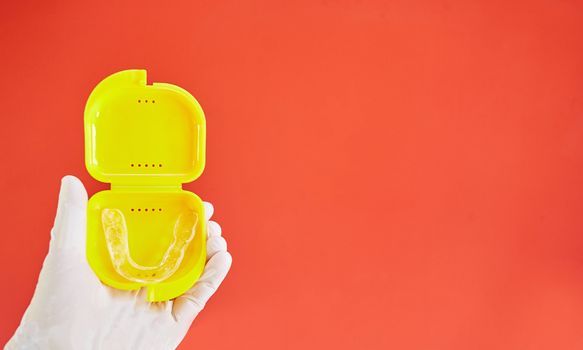 Invisible bracelets in a yellow case on a red background held in one hand by a latex glove