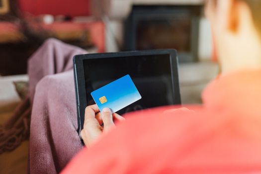 Woman lying on the sofa and shopping online from home with her tablet and credit card