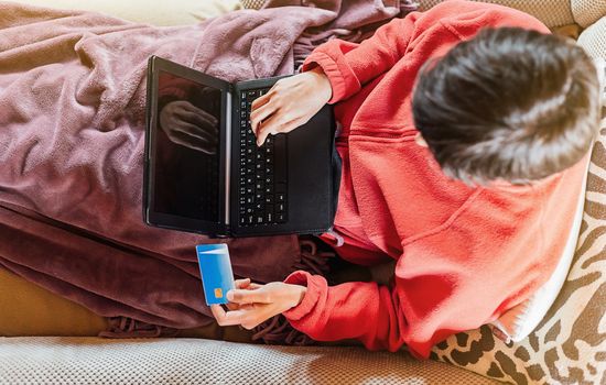 Woman lying on the sofa and shopping online from home with her tablet and credit card