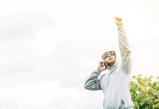 A young A young man with blue sunglasses, gray sweatshirt and beard talking on a cell phone looking up