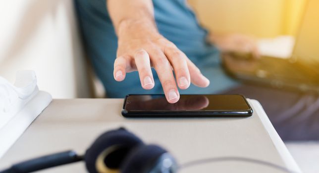 Man teleworking at home in his room with a laptop and taking the phone from the bedside table where there is also a headset