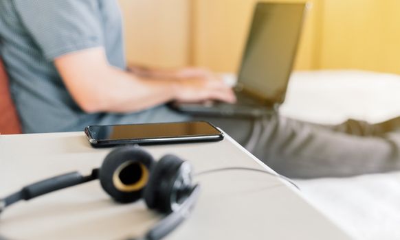 Man teleworking at home in his room with a laptop and table where there is a mobile phone and a headset