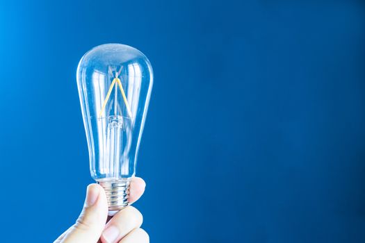 Left hand holding a light bulb on a blue background
